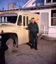 A photo of a milkman in front of his milk truck.